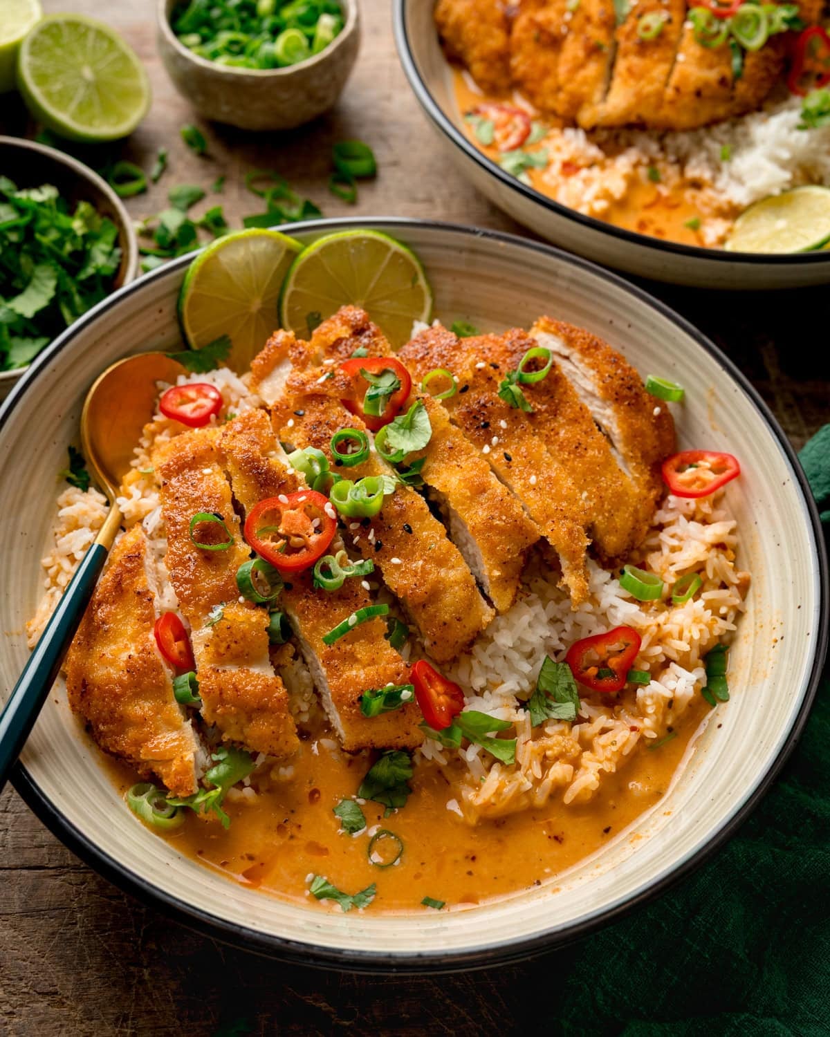 Crispy chicken and rice served in a bowl with coconut curry broth, spring onions, chilli slices, and lime wedges.