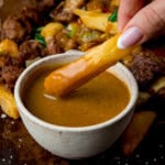 A chip being dipped into a bowl of Chinese style curry sauce with a portion of salt and pepper chicken in the background.