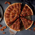 A pecan pie tart with one slice being lifted by a cake slice.