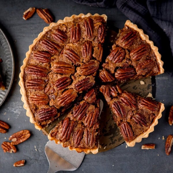 A pecan pie tart with one slice being lifted by a cake slice.