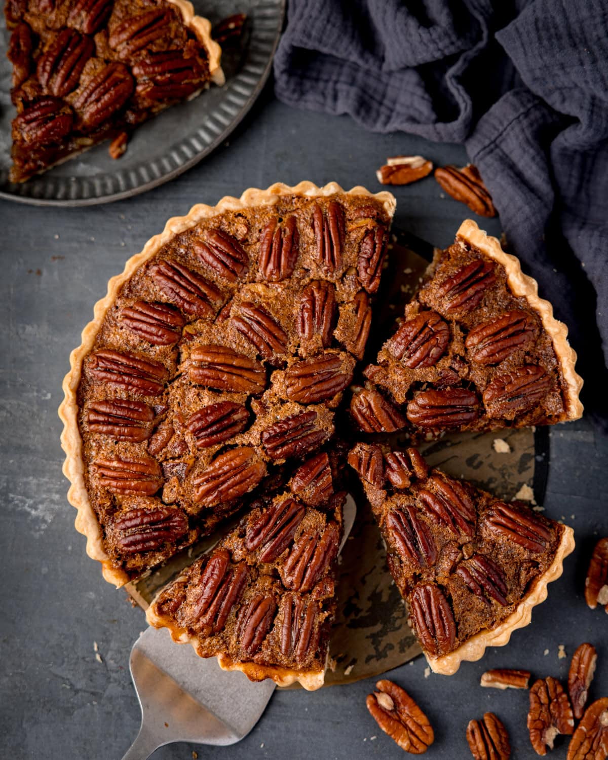 A whole pecan pie with a slice being lifted by a cake slice, and a separate slice on a small plate nearby.