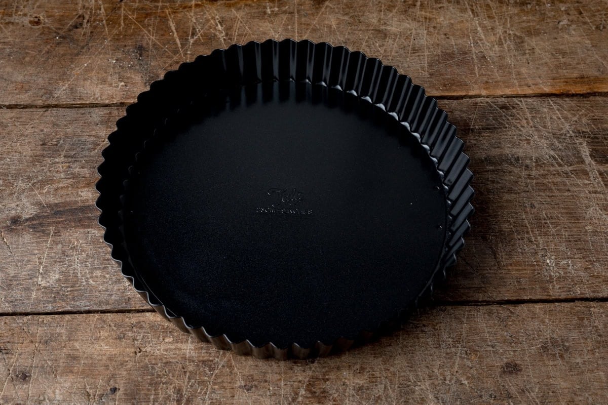 Black fluted tart tin on a wooden surface.